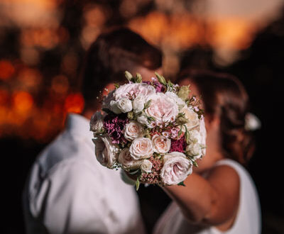 Pareja de novios besándose durante su ceremonia de boda, con el ramo de novia entre ellos, en un emotivo momento del 'Sí, quiero' al atardecer.