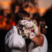 Pareja de novios besándose durante su ceremonia de boda, con el ramo de novia entre ellos, en un emotivo momento del 'Sí, quiero' al atardecer.