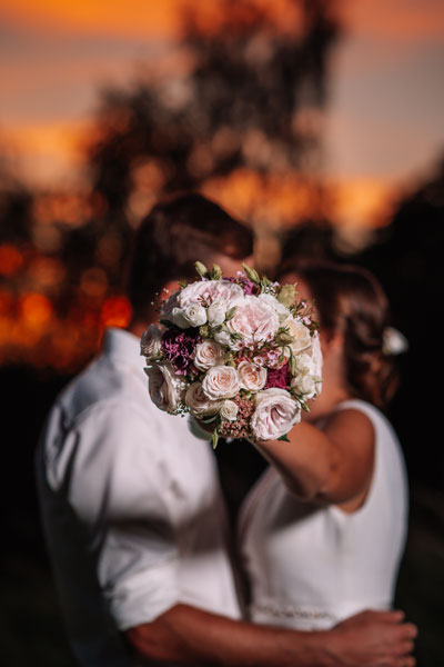 Pareja de novios besándose durante su ceremonia de boda, con el ramo de novia entre ellos, en un emotivo momento del 'Sí, quiero' al atardecer.