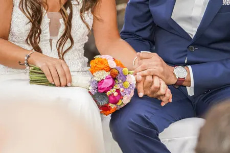 Pareja de novios sentada sosteniendo el ramo y dandose la mano