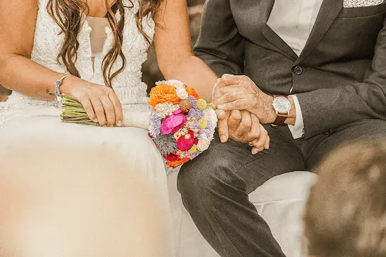 Boda de oro en Gran Canaria, una pareja mayor se toma las manos vestidos de novios con el ramo de flores